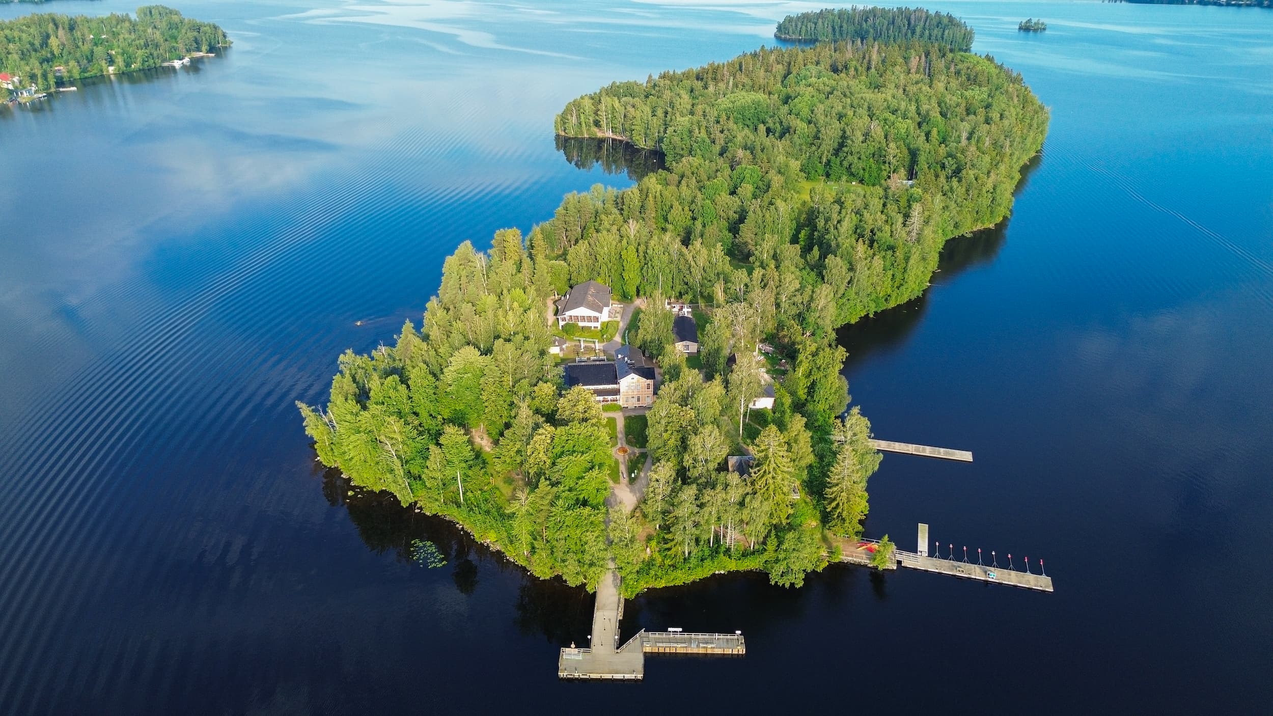 A small island in the middle of a lake with a handful of buildings and a pier.